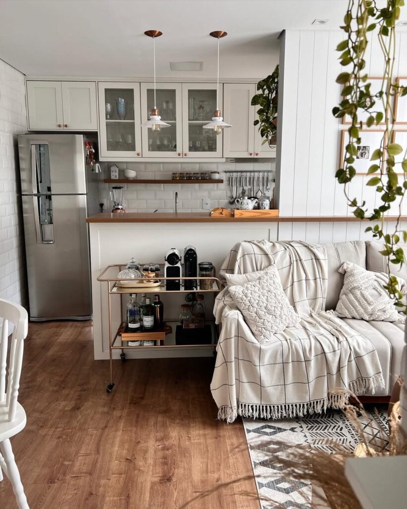 Sala e cozinha integradas em tons claros com carrinho decorativo ao lado do sofá