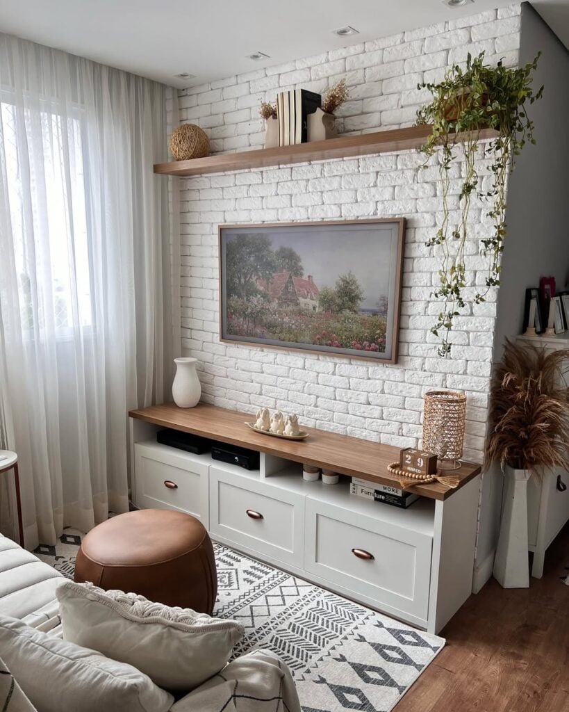 Sala de estar com rack branco com gavetas e bancada de madeira, parede de tijolinhos e prateleira de madeira