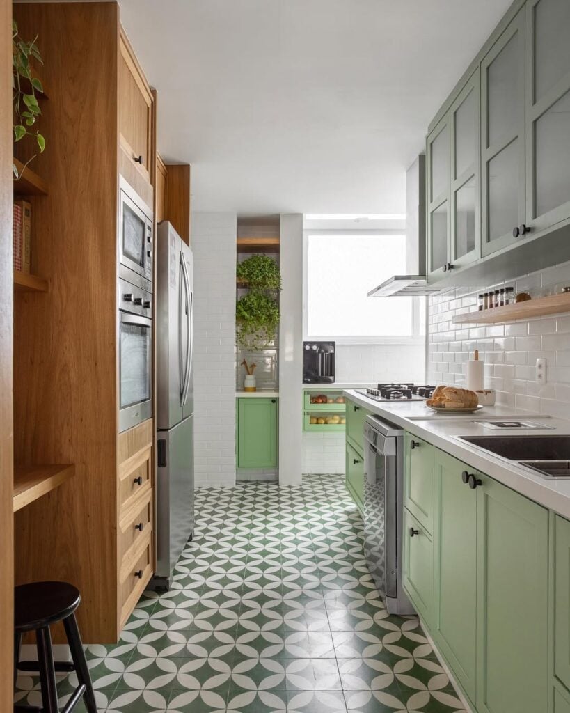 Cozinha estreita com armários verde-menta de um lado e armários na cor da madeira com eletrodomésticos embutidos, e piso com azulejo colorido