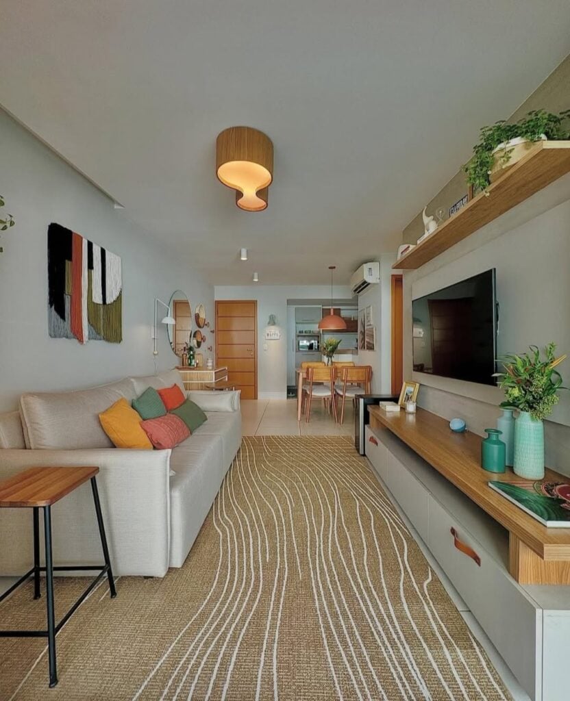 Sala de estar com sofá claro, almofadas coloridas, tapete bege com linhas brancas