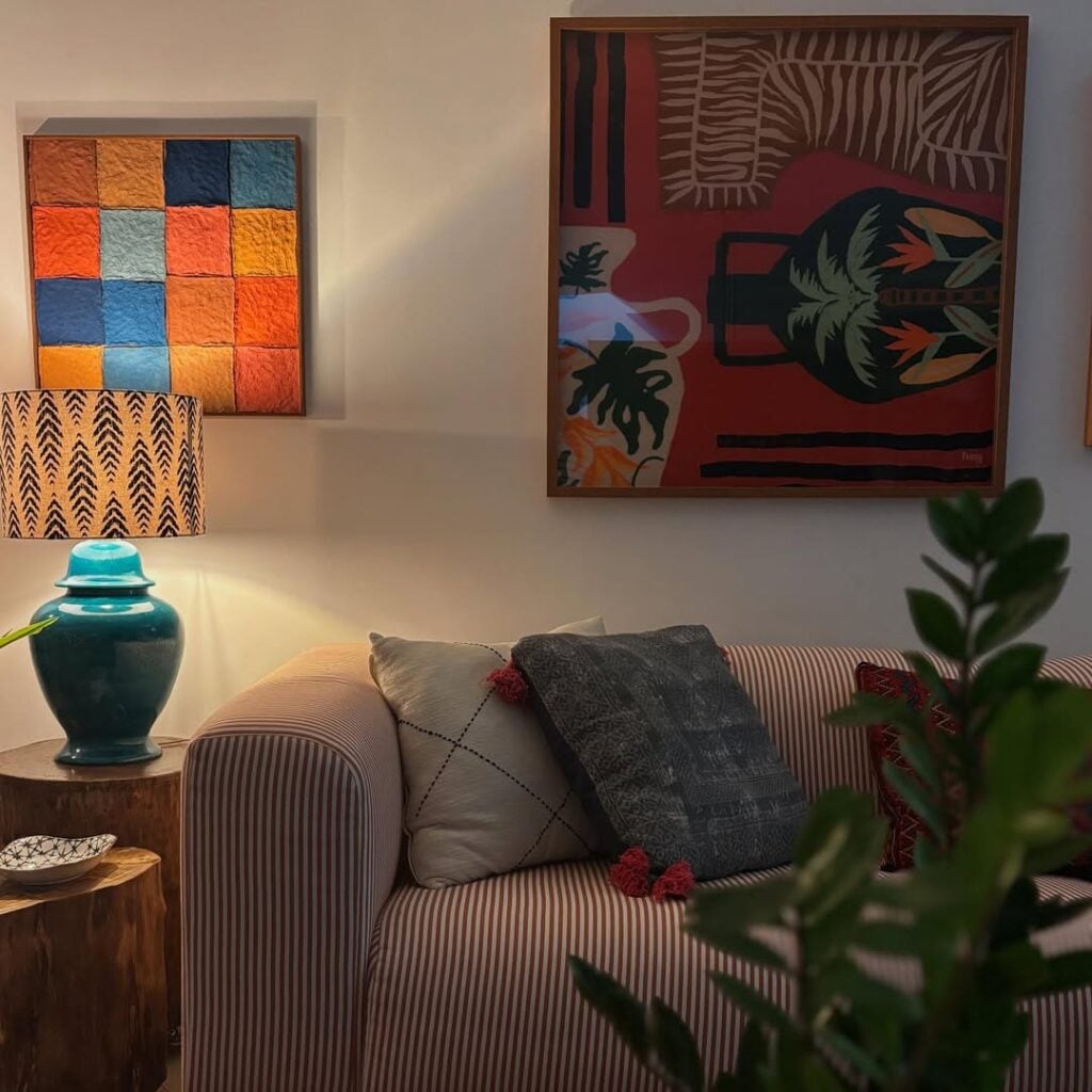 Sala com sofá listrado, quadros coloridos e abajur com base azul