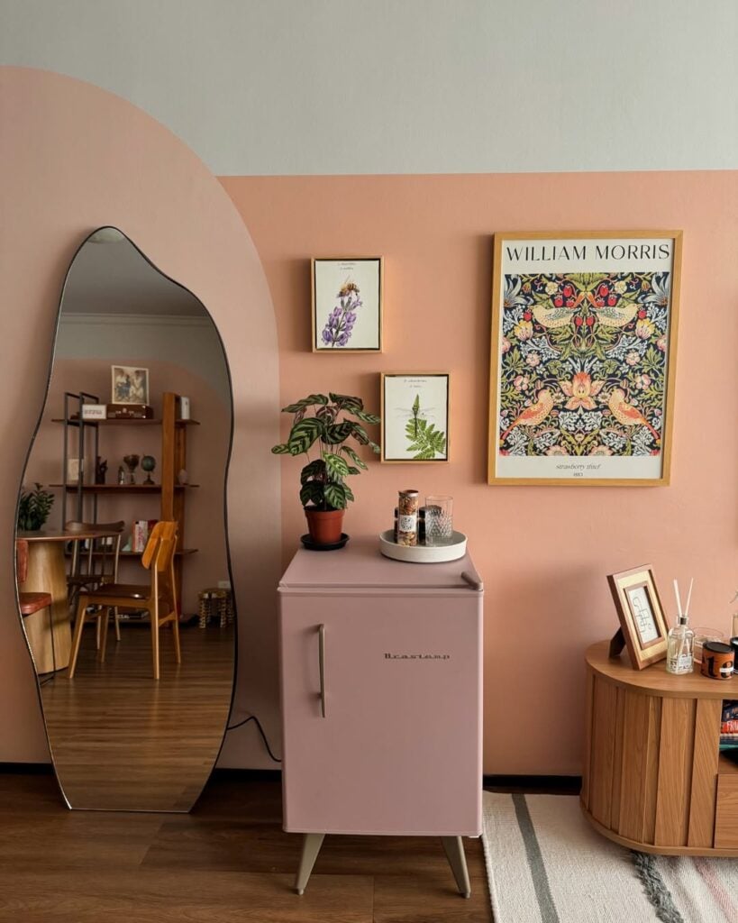 Ambiente com paredes coloridas, quadros, frigobar rosa e espelho orgânico