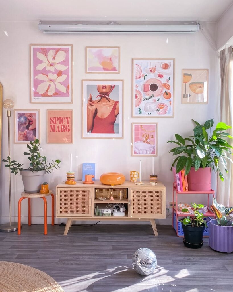 Ambiente com parede clara, quadros coloridos, rack de palhinha e plantas