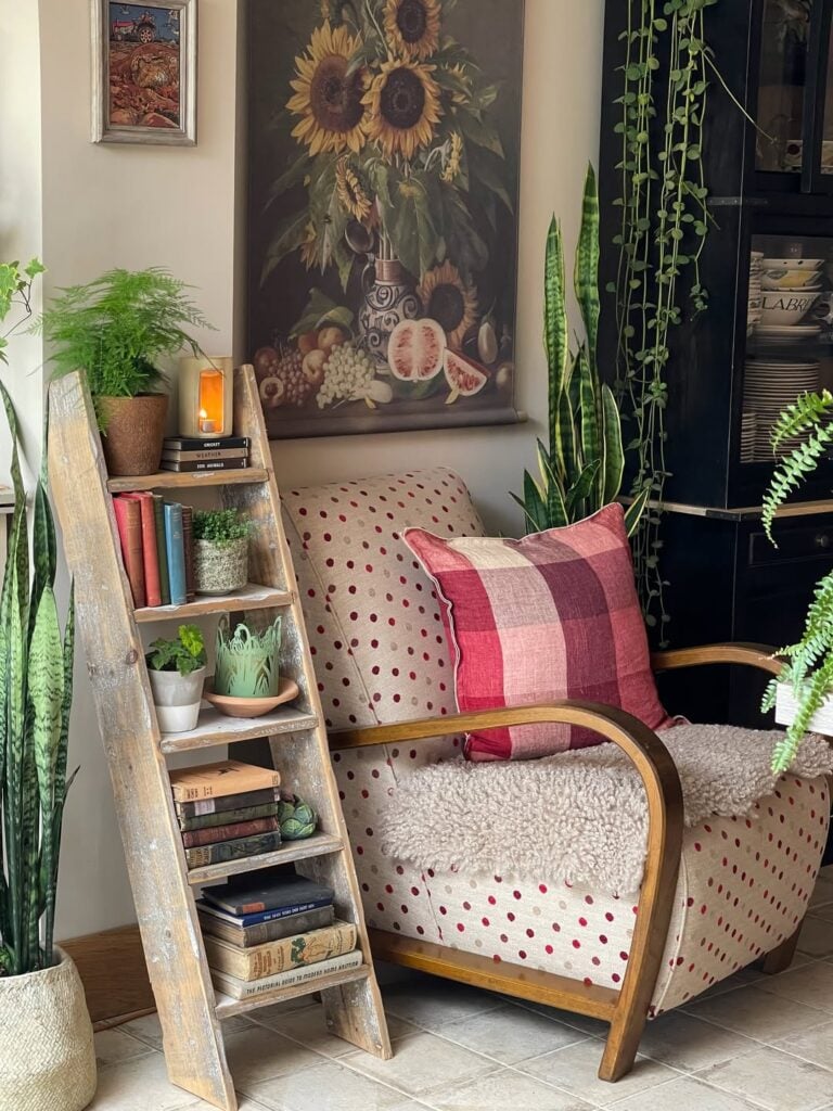Cantinho com poltrona clara com bolinhas vermelhas, plantas e escada rústica com livros e vasinhos