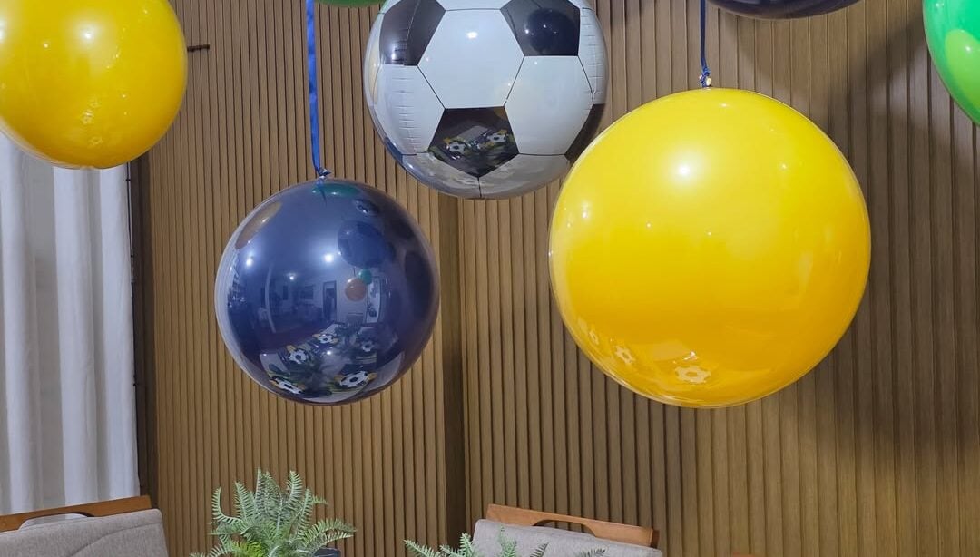 Mesa posta em verde, amarelo e azul e balões coloridos pendurados