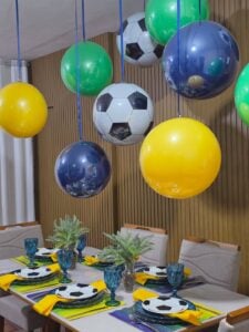 Mesa posta em verde, amarelo e azul e balões coloridos pendurados