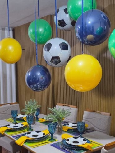 Mesa posta em verde, amarelo e azul e balões coloridos pendurados