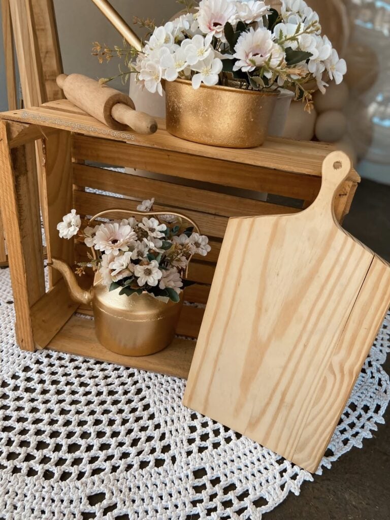 Decoração de chá de cozinha com guardanapo de crochê branco, caixote de madeira, tábua de carne, rolo e chaleira e panela douradas com flores brancas