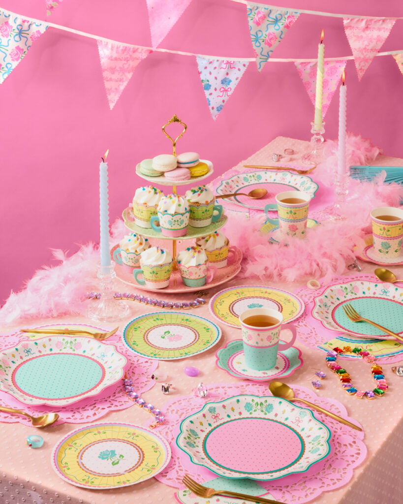 Mesa posta com toalha rosa, pratinhos coloridos, cupcakes e macarrons