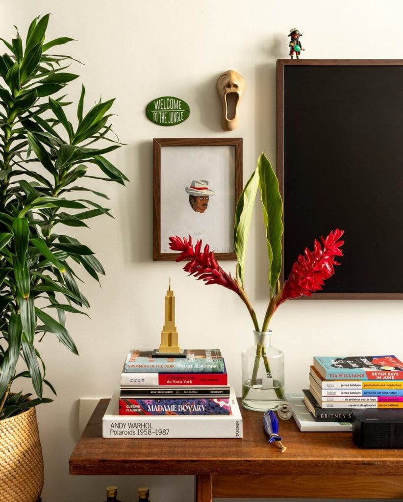 Banco de madeira com livros empilhados e vaso com flores vermelhas