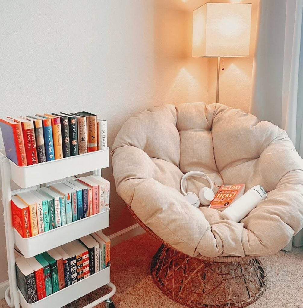 Cantinho com poltrona confortável, luminária de piso e carrinho branco com livros