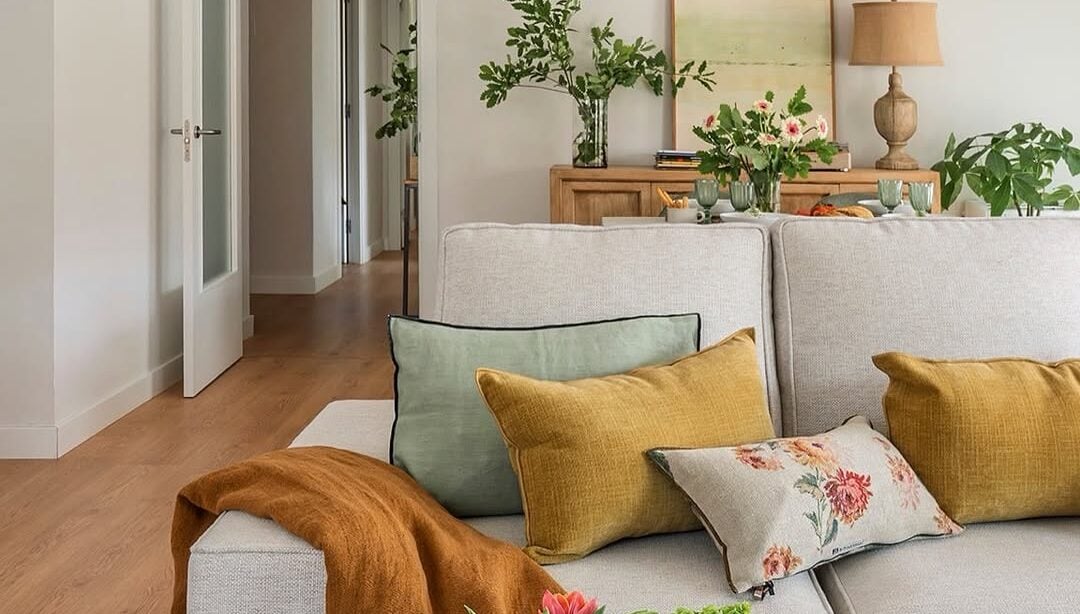 Sala de estar com sofá claro, almofadas coloridas e mesa de centro com flores rosa