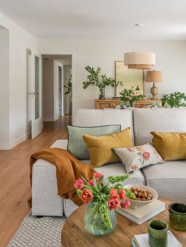 Sala de estar com sofá claro, almofadas coloridas e mesa de centro com flores rosa