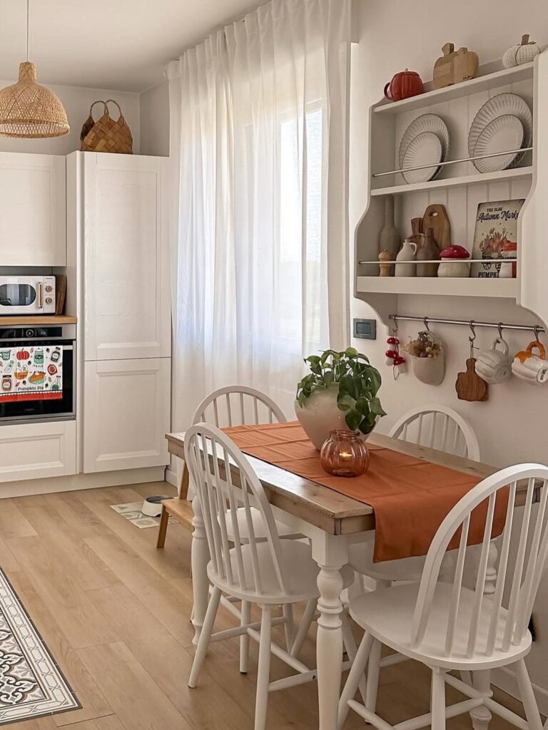 Mesa com cadeiras brancas de madeira e prateleira com pratos e outros objetos