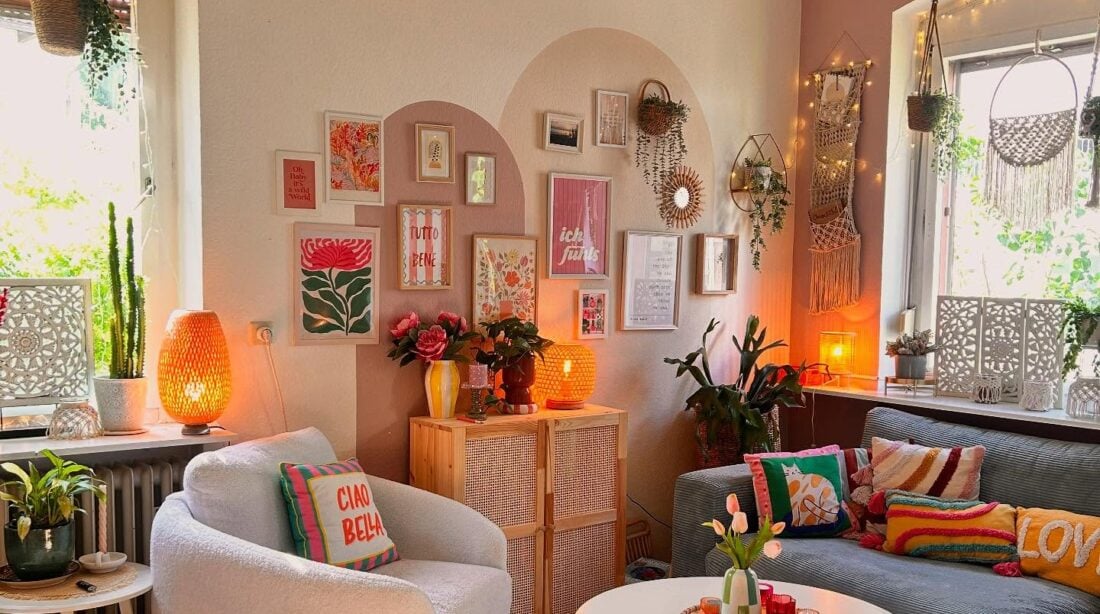 Sala aconchegante com sofá cinza, poltrona clara, pintura orgânica na parede com quadros, luminária de fibras naturais