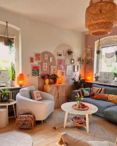 Sala aconchegante com sofá cinza, poltrona clara, pintura orgânica na parede com quadros, luminária de fibras naturais