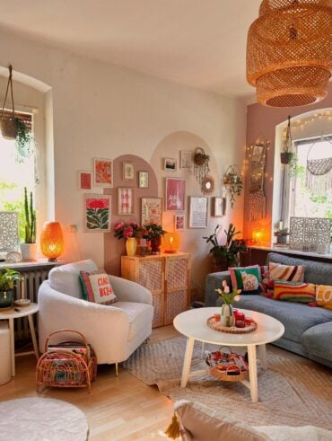 Sala aconchegante com sofá cinza, poltrona clara, pintura orgânica na parede com quadros, luminária de fibras naturais