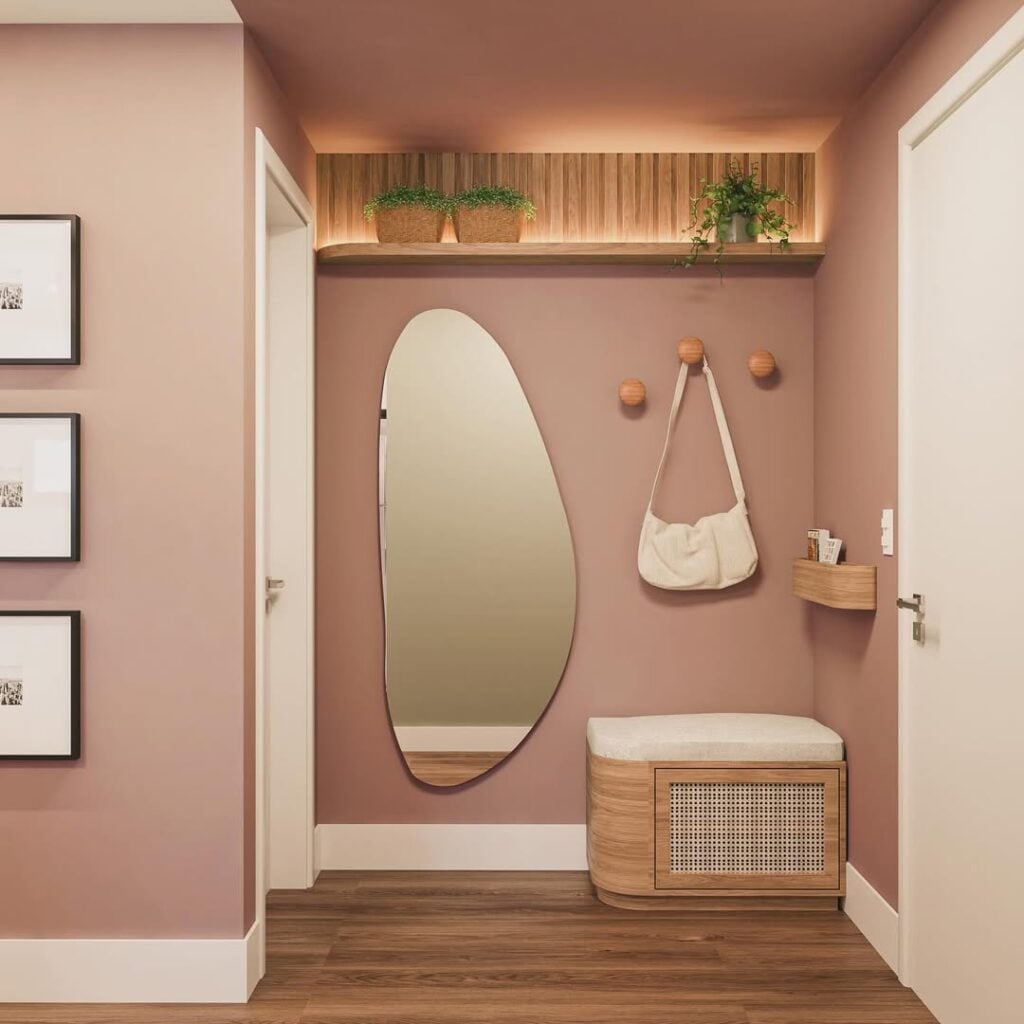 Hall de apartamento com a parede rosa, espelho orgãnico, banco e suporte para bolsas