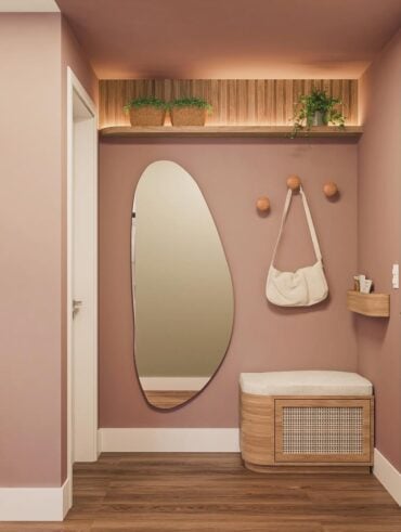Hall de apartamento com a parede rosa, espelho orgãnico, banco e suporte para bolsas