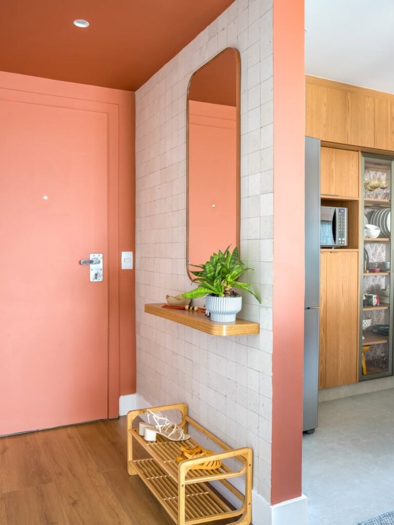 Hall de apartamento com parede branca, prateleira, espelho e sapateira