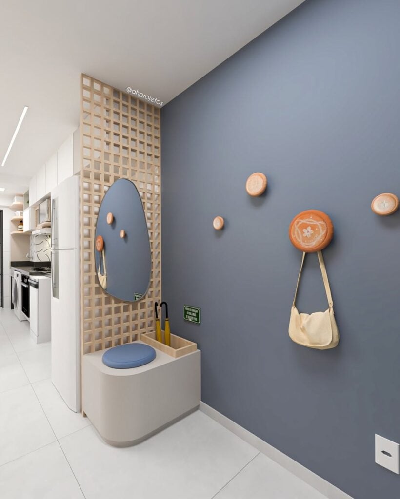 Hall de entrada com parede azul, suporte para bolsas e casados, banco pequeno e espelho em painel de muxarabi