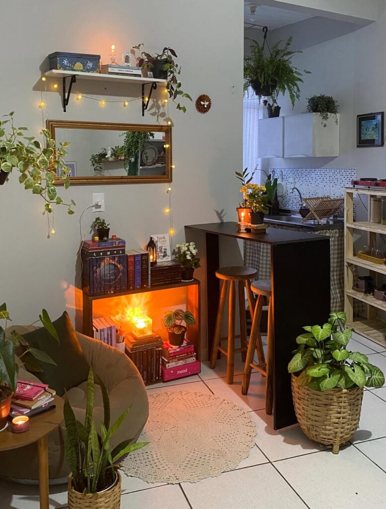 Ambiente com poltrona, almofada, estante pequena com livros e plantas