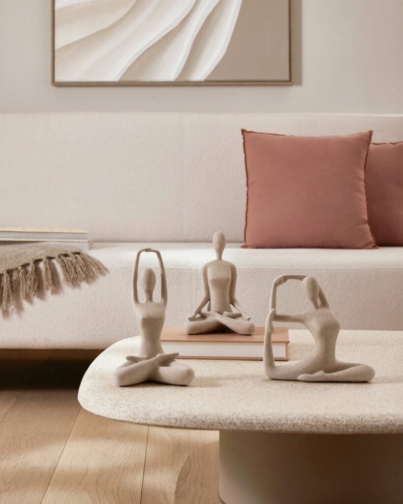 Sala com sofá claro e mesa de centro com libro e esculturas em posição de yoga