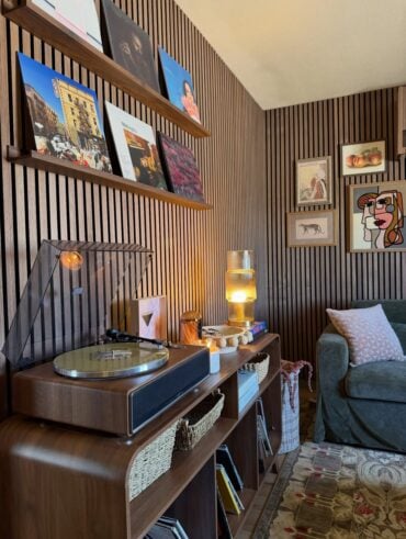 Sala de estar com paineis ripados na parede, prateleira com discos e móvel de madeira com vitrola