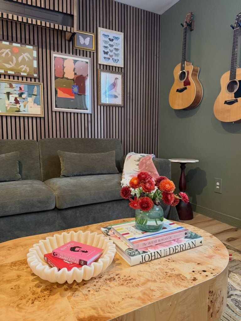 Sala de estar com sofá cinza, parede ripada com quadros e parede escura com dois violões
