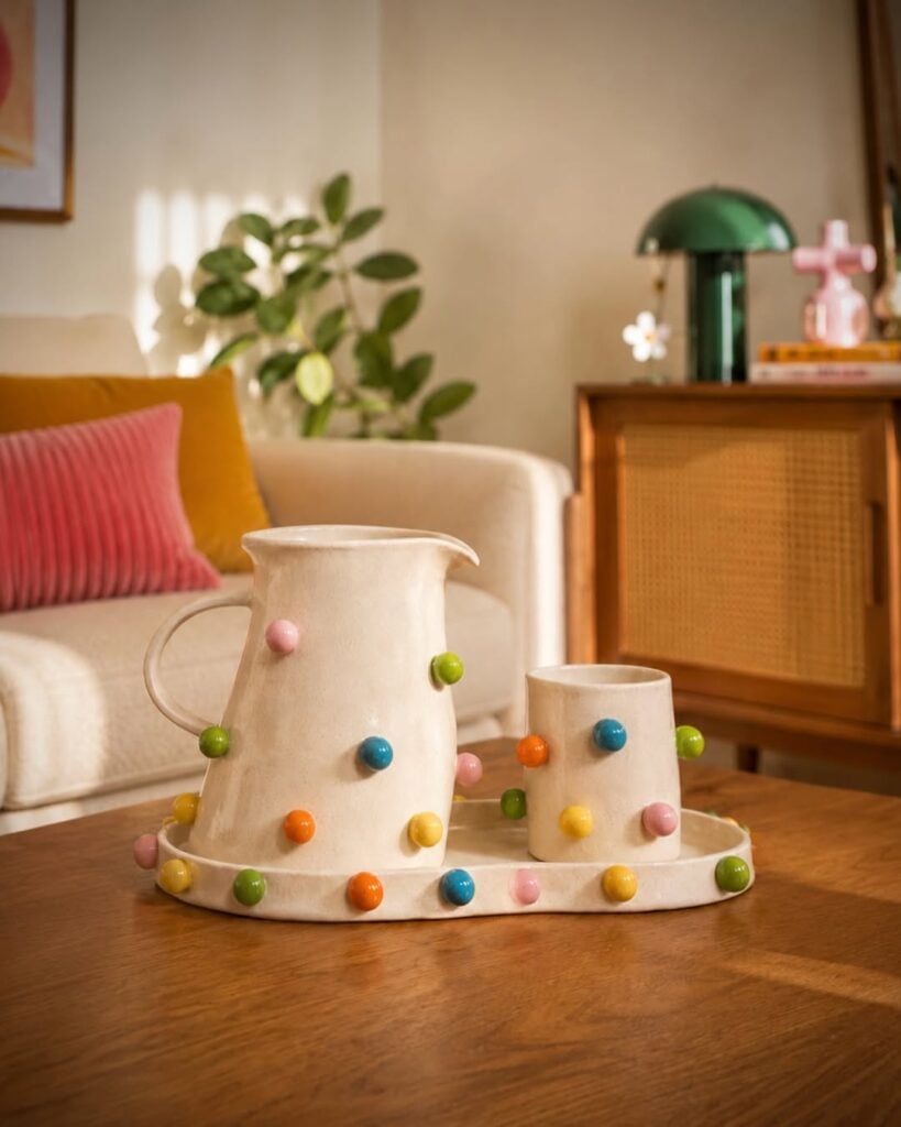 Sala de estar com sofá claro, mesa de madeira com bandeja, jarra e caneca de cerâmica clara com bolinhas coloridas