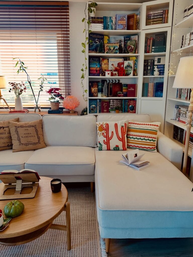 Sala de estar com sofá claro, almofadas coloridas, estante branca com livros e objetos decorativos
