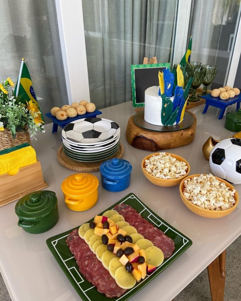 Mesa decorada para Copa, com panelinhas em verde, amarelo e azul, e pratinhos com dezenhos de bola