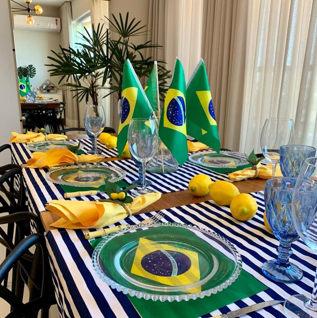Mesa posta para Copa: caminhos de mesa listrados em branco e azul, bandeirinhas do Brasil, taças azuis e limões sicilianos