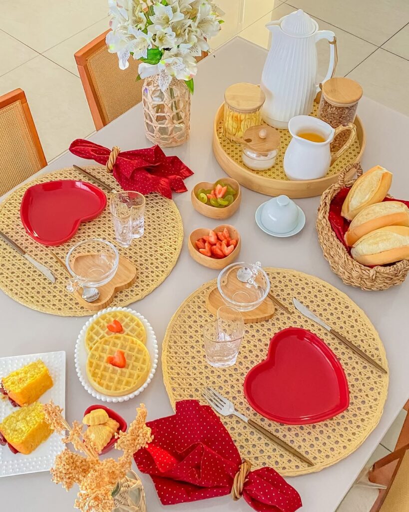 Mesa posta com sousplats de palhinha, pratos e copos em formato de coração e guardanapos vermelhos