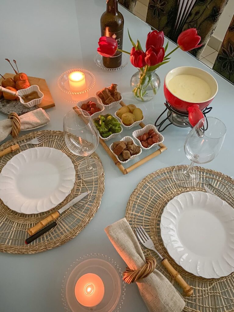 Mesa posta de Dia dos Namorados com pratos brancos, vaso com tulipas e fondue