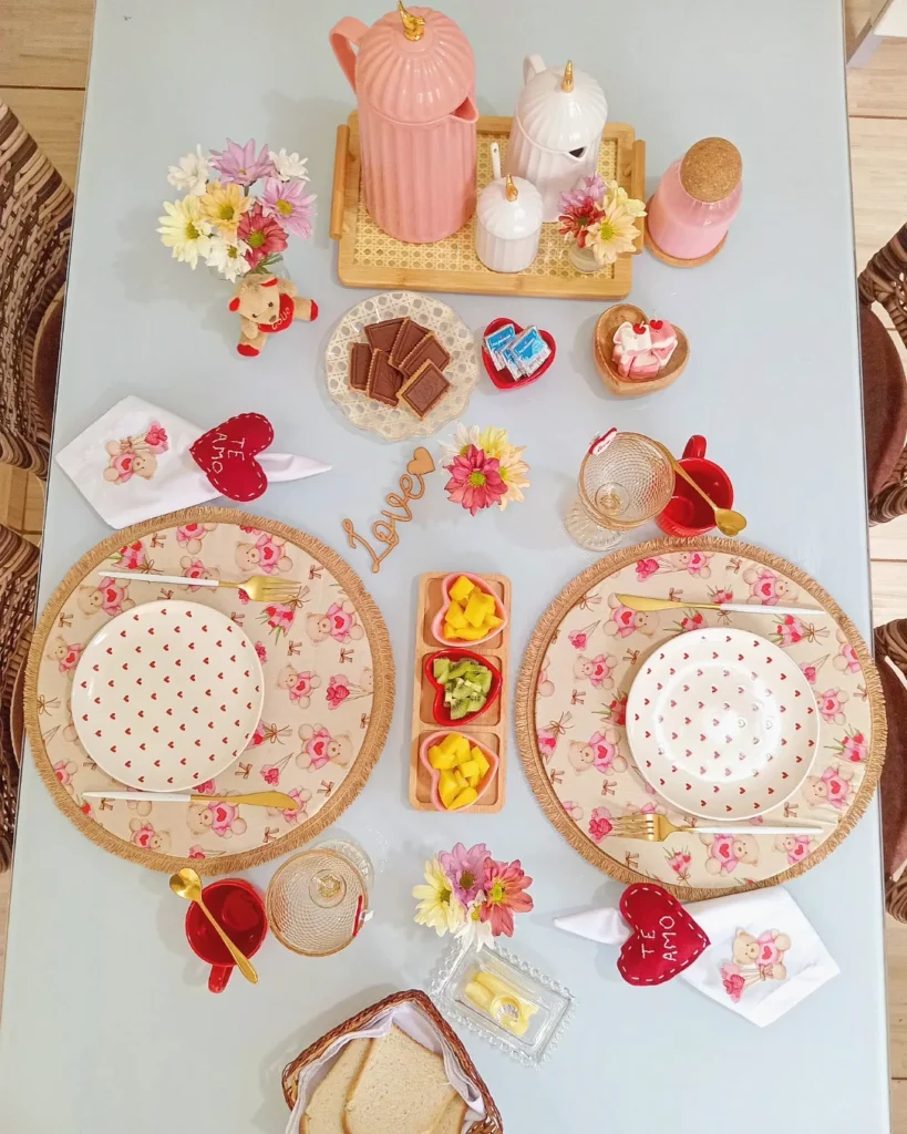 Mesa posta de Dia dos Namorados com sousplats de rosas, pratos brancos com corações vermelhos e xícaras vermelhas