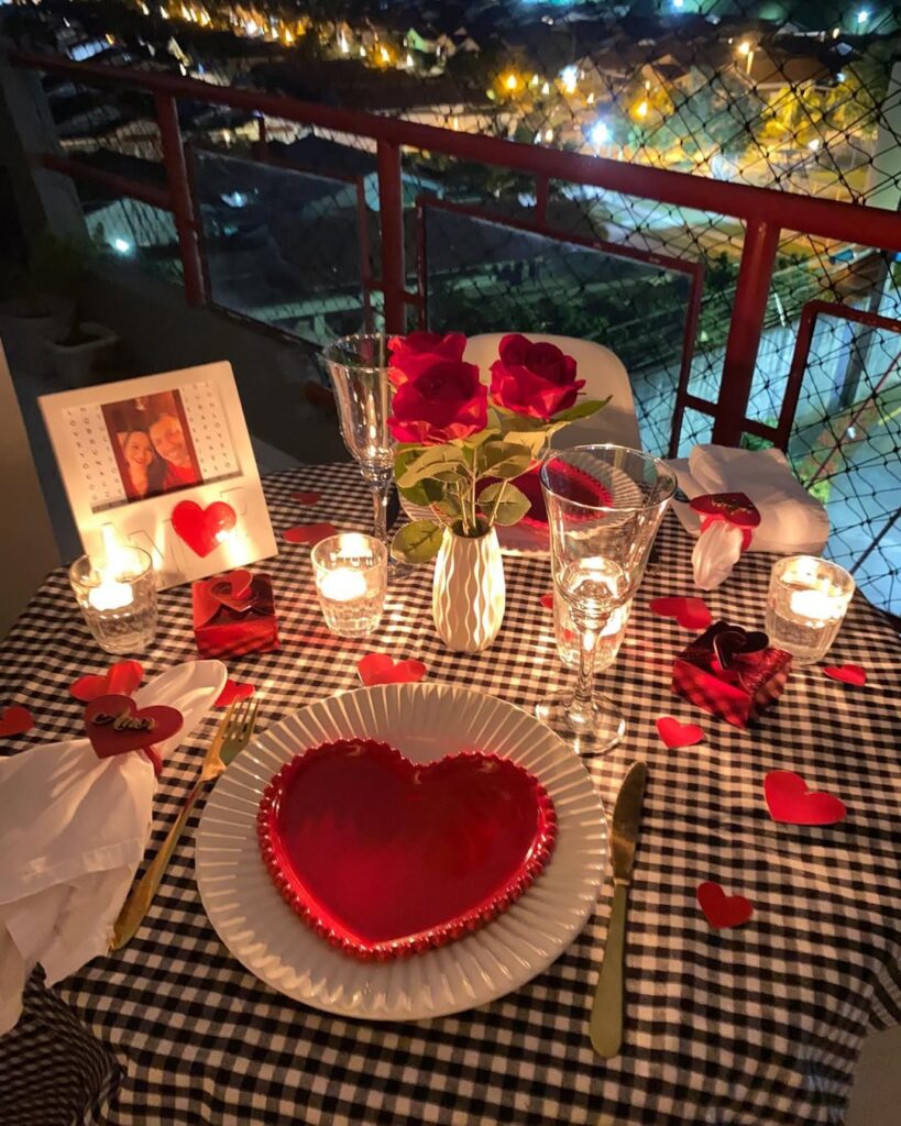 Mesa posta de Dia dos Namorados com toalha xadrez, pratos brancos e vermelhos, velas e vaso com rosas vermelhas