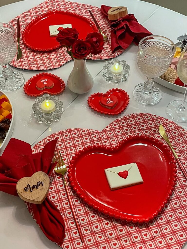 Mesa posta de Dia dos Namorados com sousplats e pratos em formato de coração, velas baixas e vaso com rosas