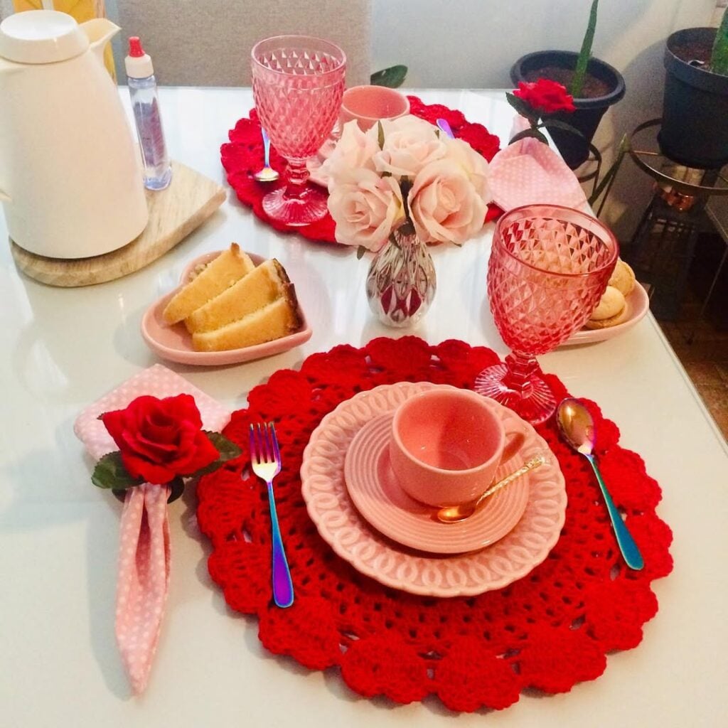Mesa posta rosa e vermelho com sousplats de crochê vermelho e louças rosa claro