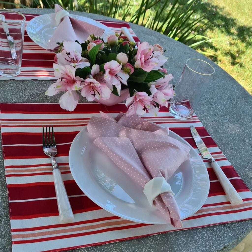 Mesa posta com pratos brancos, guardanapos rosa e jogos americanos listrados de vermelho e branco