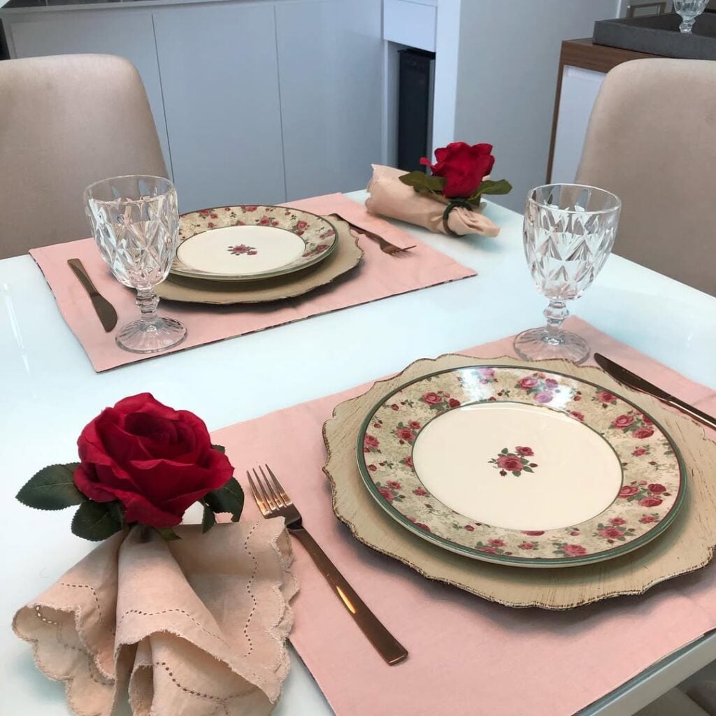 Mesa posta de Dia dos Namorados com jogos americanos rosa, pratos com flores e guardanapos com anel de rosa