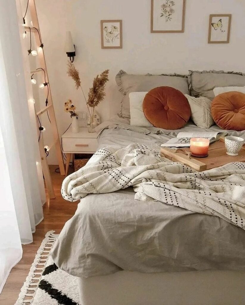 Cama com várias almofadas, manta, bandeja de maderia com chá e vela