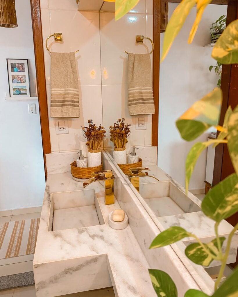 Banheiro branco com bancada marmorizada e suporte de metal dourado para toalha
