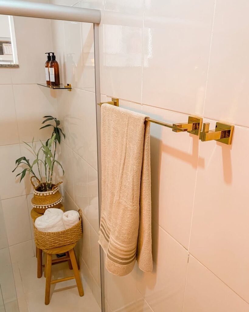 Banheiro branco com bancada marmorizada e suporte de metal dourado para toalha