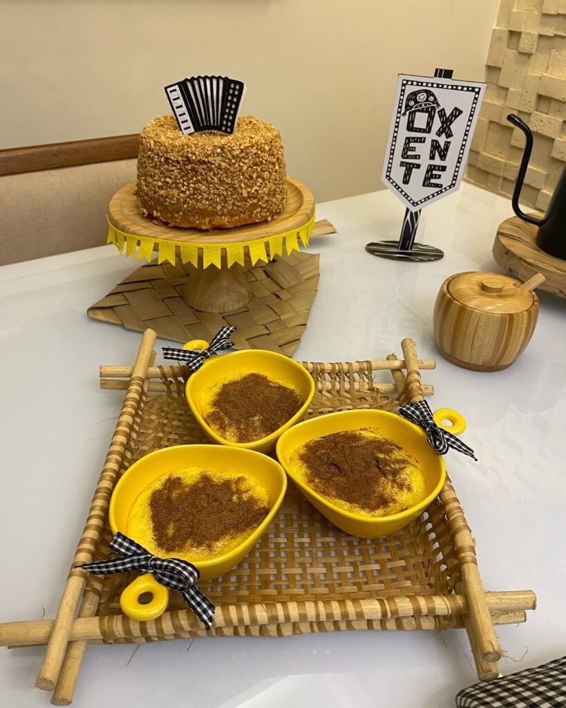 Mesa juninha com pratinhos amarelos, mingau e canela e bolo com amendoim