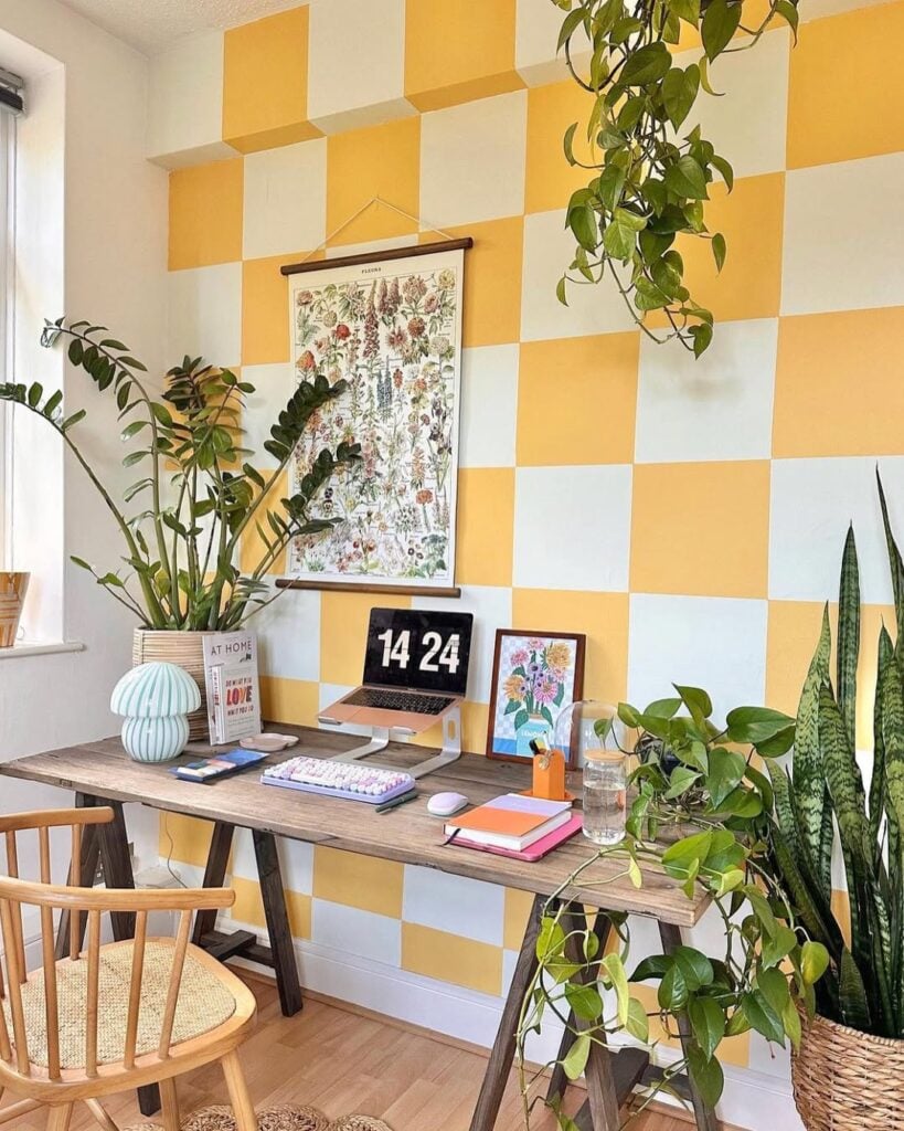 Home office com mesa e cadeira de madeira, plantas e parede quadriculada em amarelo e branco