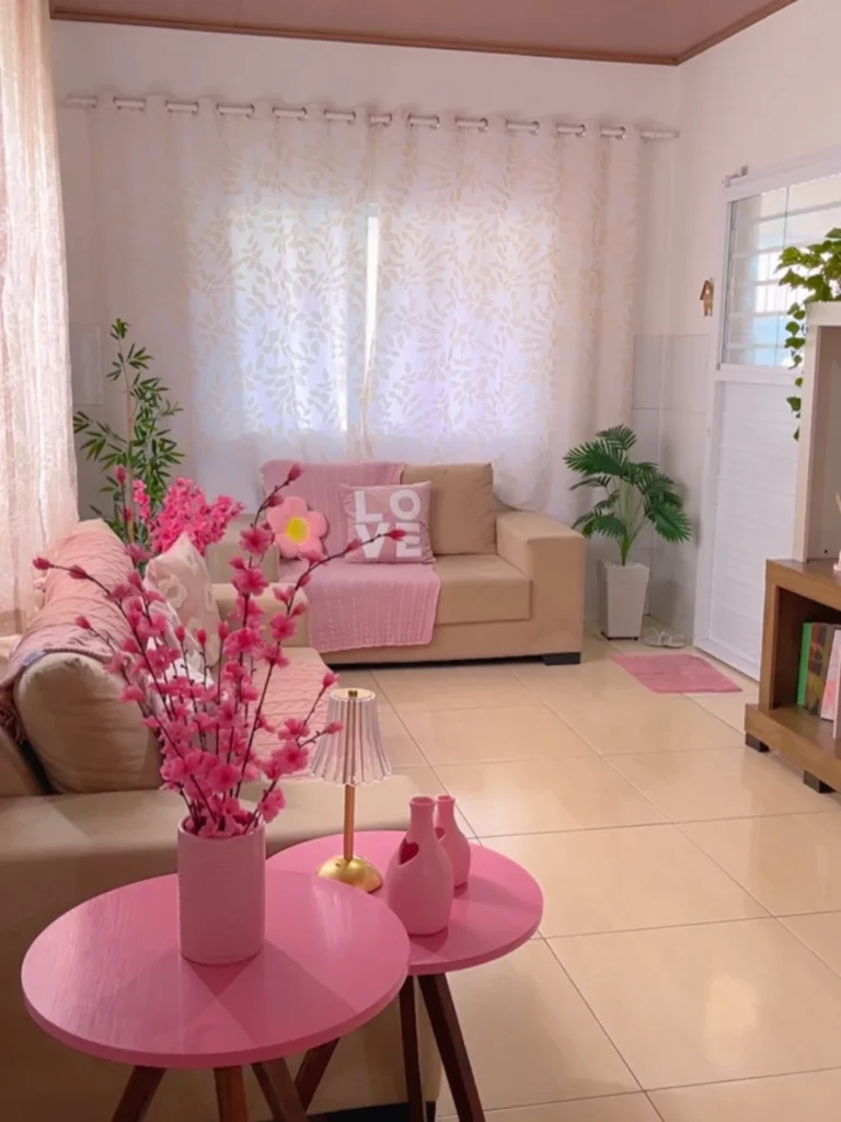 Sala com sofás claros, cortina branca, mesinhas, manta e outros itens em rosa claro