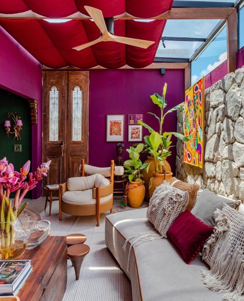 Sala com paredes roxas e pedra, poltronas, plantas e texturas