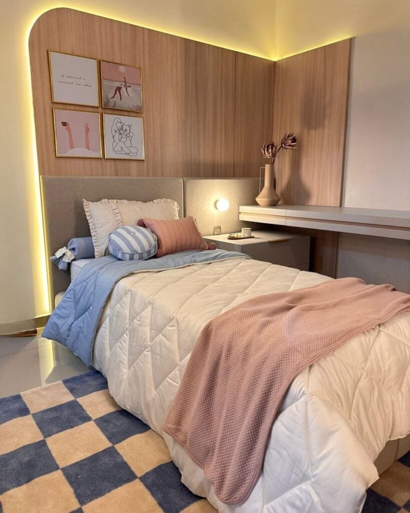 Quarto aconchegante com cama de solteiro, almofada, manta e tapete, além de móvel sob medida na cabeceira, bancada e mesa lateral