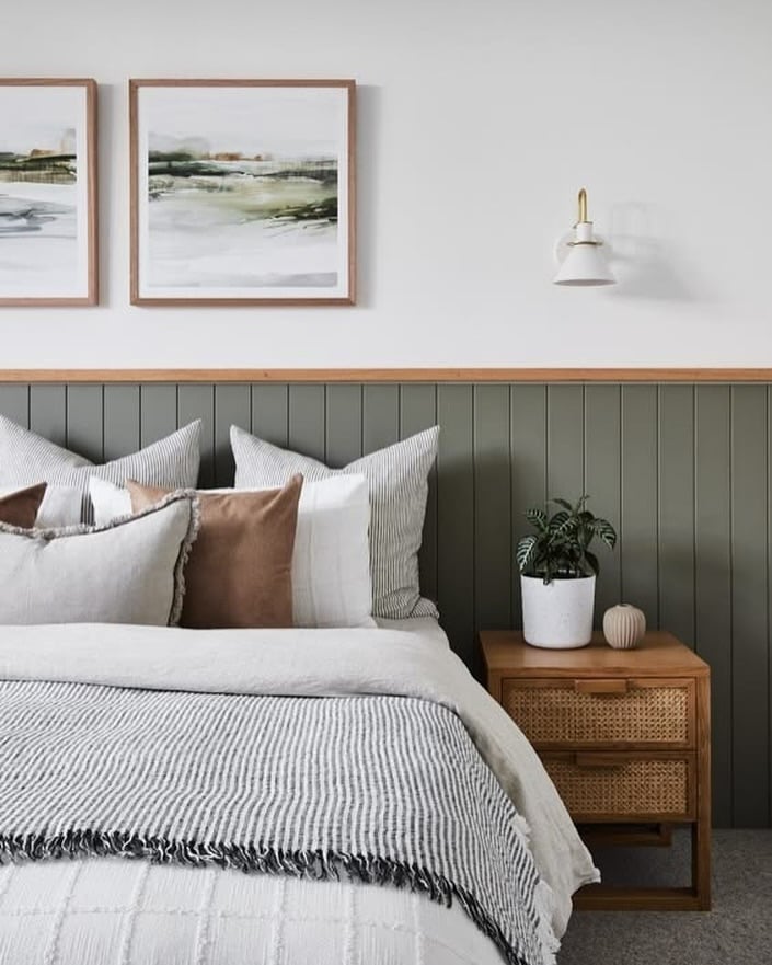 Quarto aconchegante com cama de casal, almofada, além de móvel solto na mesa lateral e cabeceira de madeira, com quadros e luminária na parede
